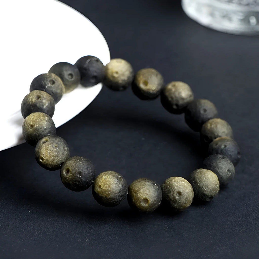 Natural obsidian crater ball bracelet with textured beads in gold or silver stone finish on a wrist.