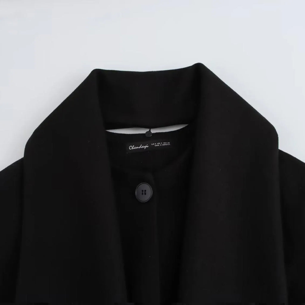 Women's long black overcoat with a grey fur collar and pockets, shown on a model.