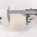 A white wool felt drying ball for laundry next to a plain cotton storage bag on a blue background.