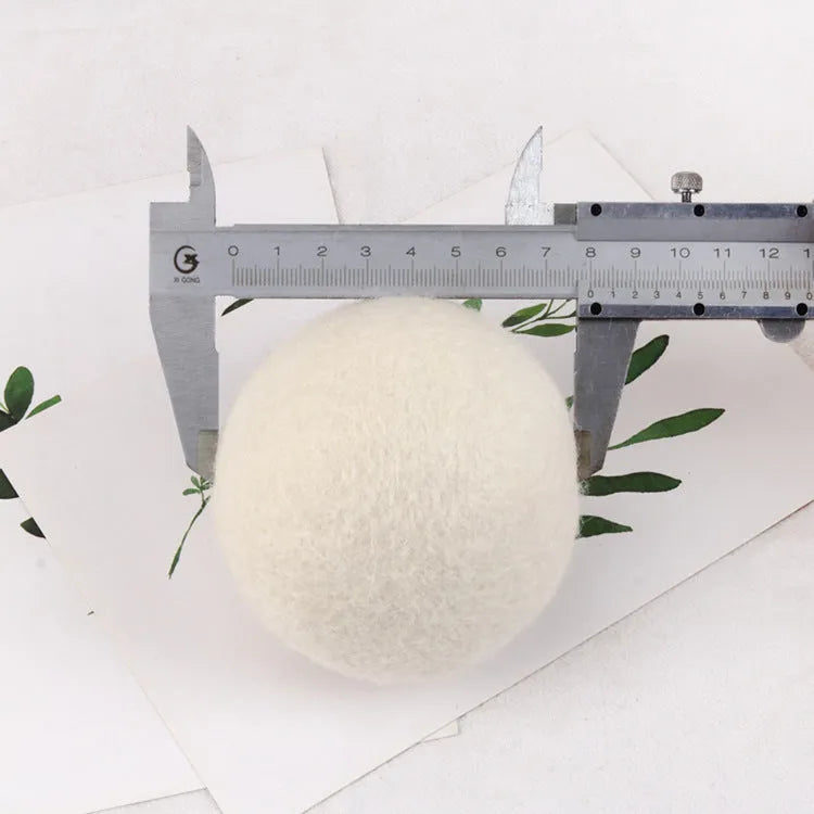 A white wool felt drying ball for laundry next to a plain cotton storage bag on a blue background.