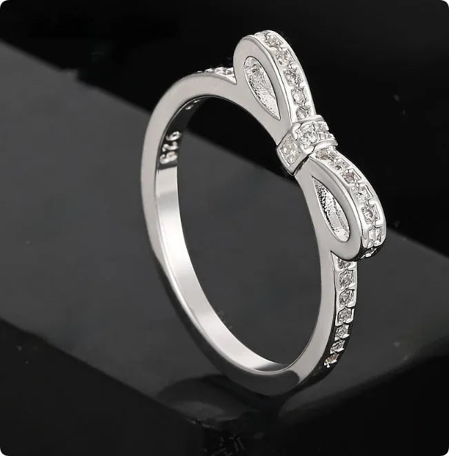 Silver coloured bow-shaped ring with sparkling rhinestone zircon crystals on a finger.