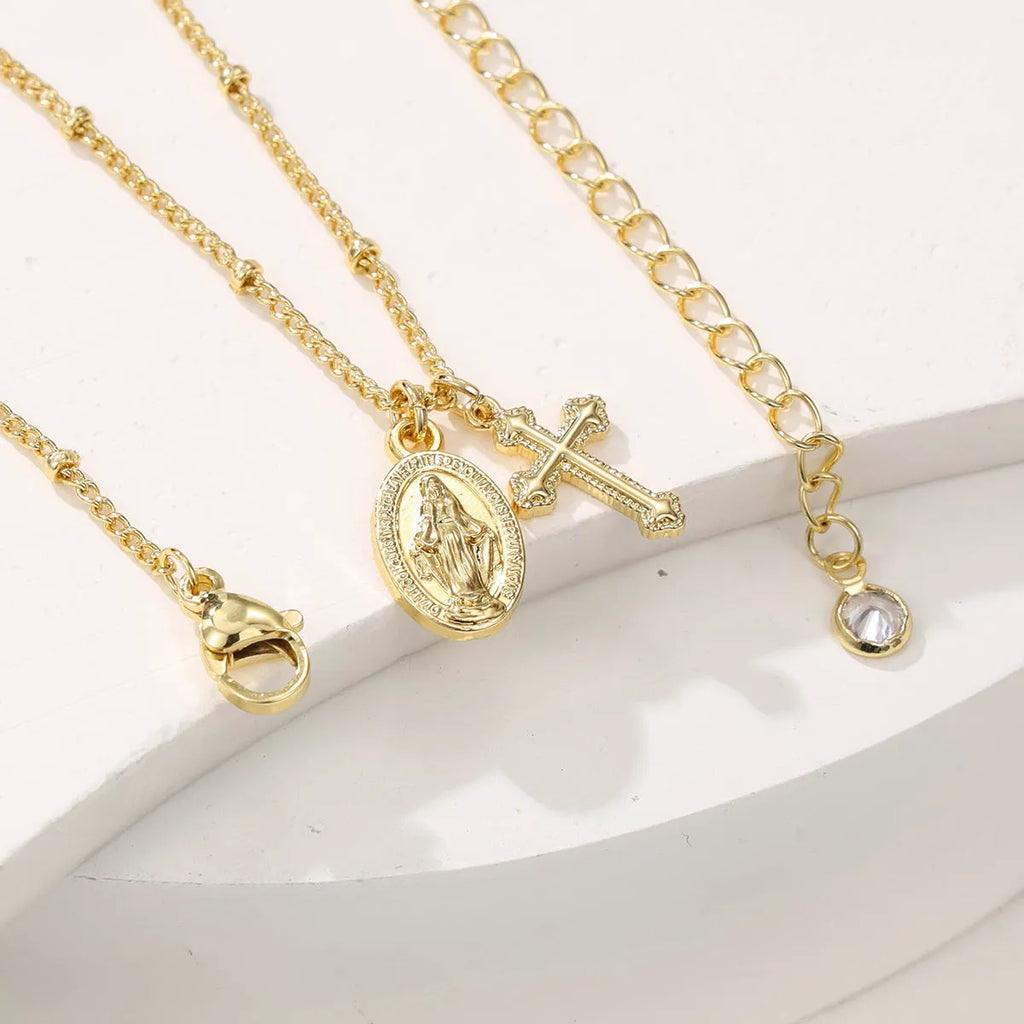 Gold coloured geometric cross necklace with a Virgin Mary ornament on a chain.