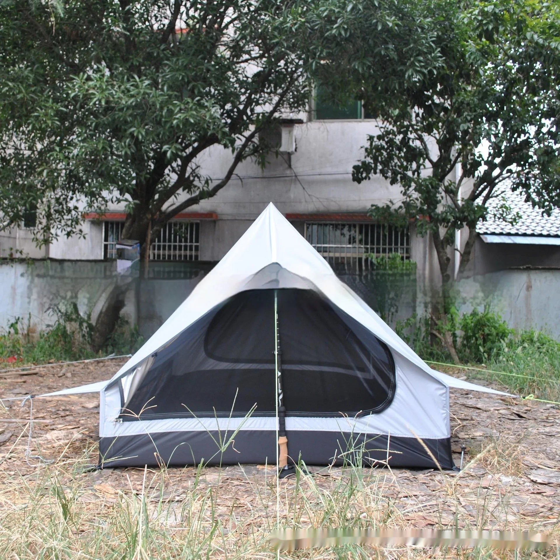 Brown ultralight A-frame hiking tent pitched with hiking poles in an outdoor setting