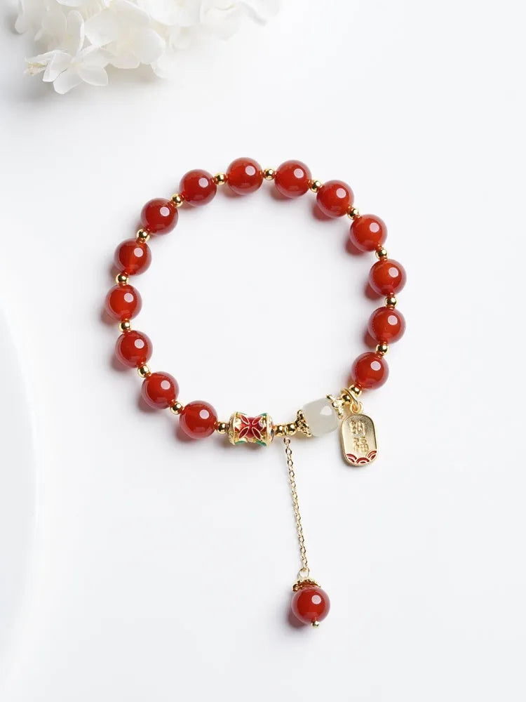 A women's bracelet with red agate beads and gold-plated metal elements on a wrist.