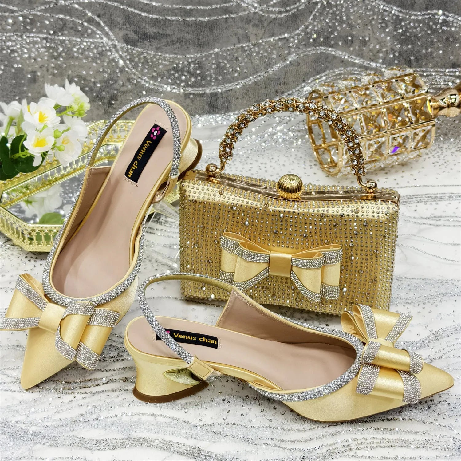 Women's black pointed sandals with a square rhinestone buckle and mid heel, next to a matching clutch bag.
