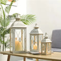 Black gold wrought iron floor standing storm lantern with tempered glass panels on a stone patio.