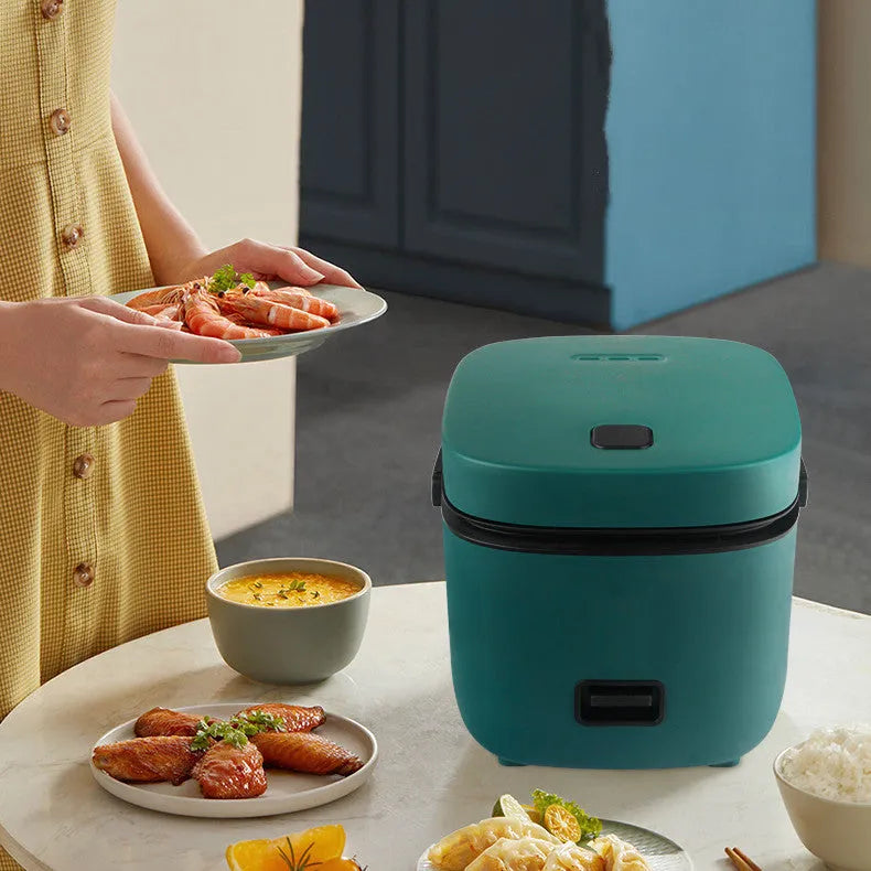 Green 1.2L mini rice cooker with metal body, button controls, and steaming plate on a worktop.