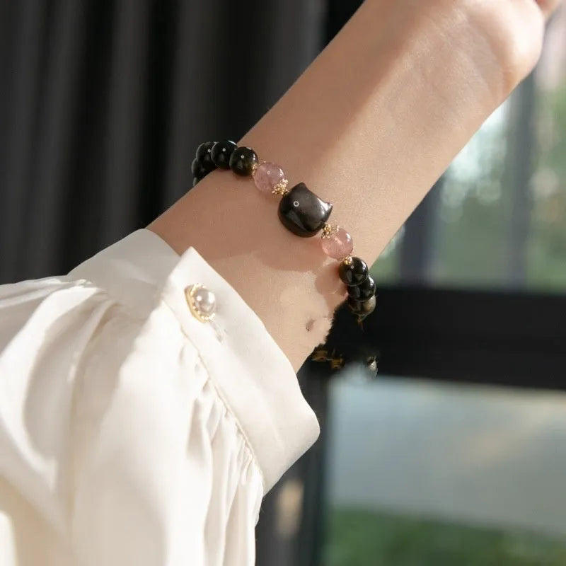 Black obsidian beaded bracelet with silver kitty cat charms on a wrist.