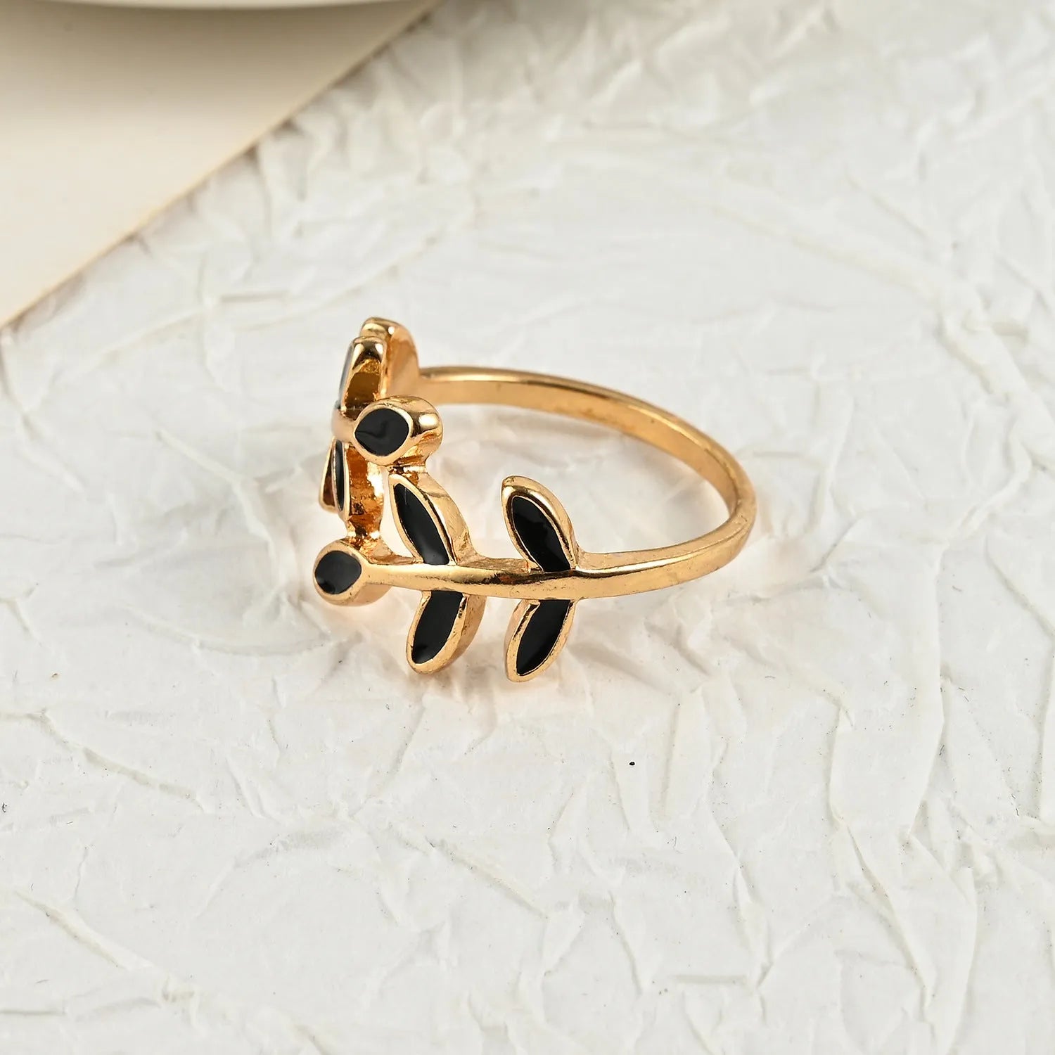 Gold-coloured acrylic ring with a geometric leaf and floral design on a white background.