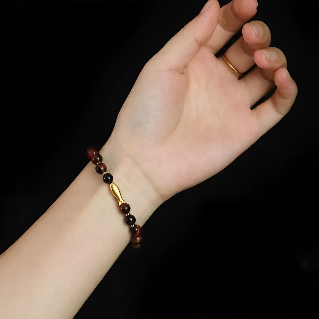 Close-up of a women's bracelet with small fish-shaped Tiger Eye stone beads in yellow, red, or gold colours.
