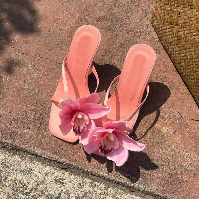 Pink women's sandals with a satin upper, artificial white Phalaenopsis flower, square toe, and a mid heel.