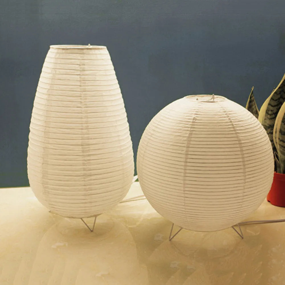 White handcrafted rice paper table lamp with either a circular or rectangular shade on a wooden desk.