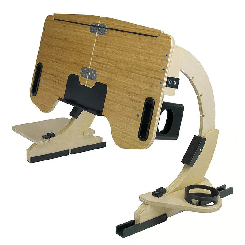 A wooden folding computer table with adjustable angle, shown in a neutral colour on a bed.