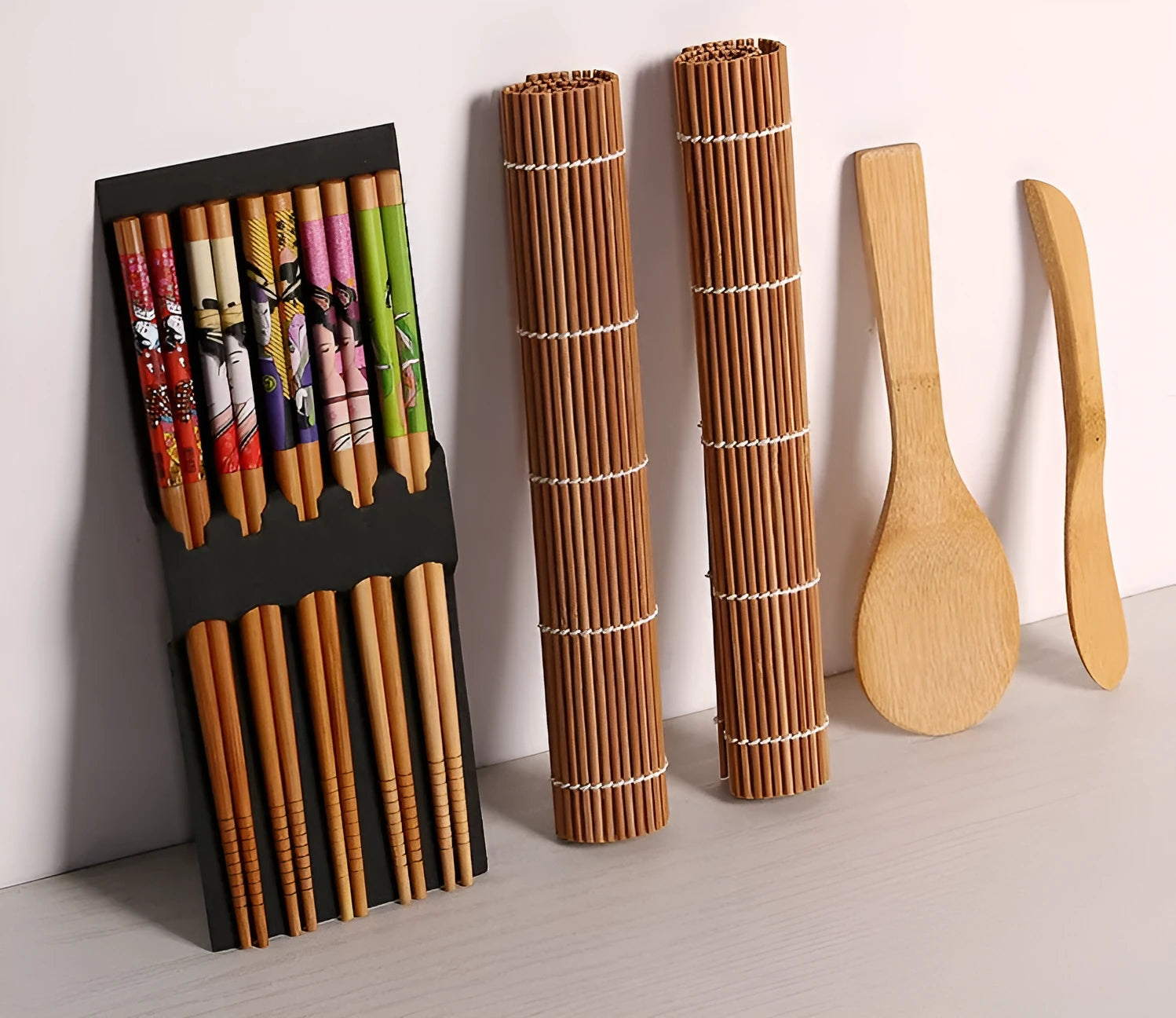 White sushi tool set with bamboo rolling mat, rice paddle, and sushi mold on a surface.