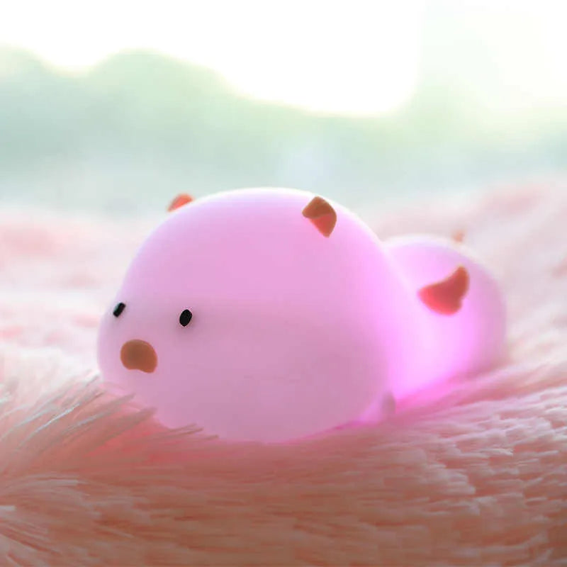 Blue silicone pig-shaped rechargeable LED night light with touch control on a wooden surface.