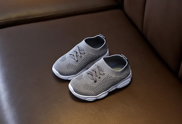 Children's white fabric lazy slip-on shoe with a non-slip rubber sole on a wooden floor.