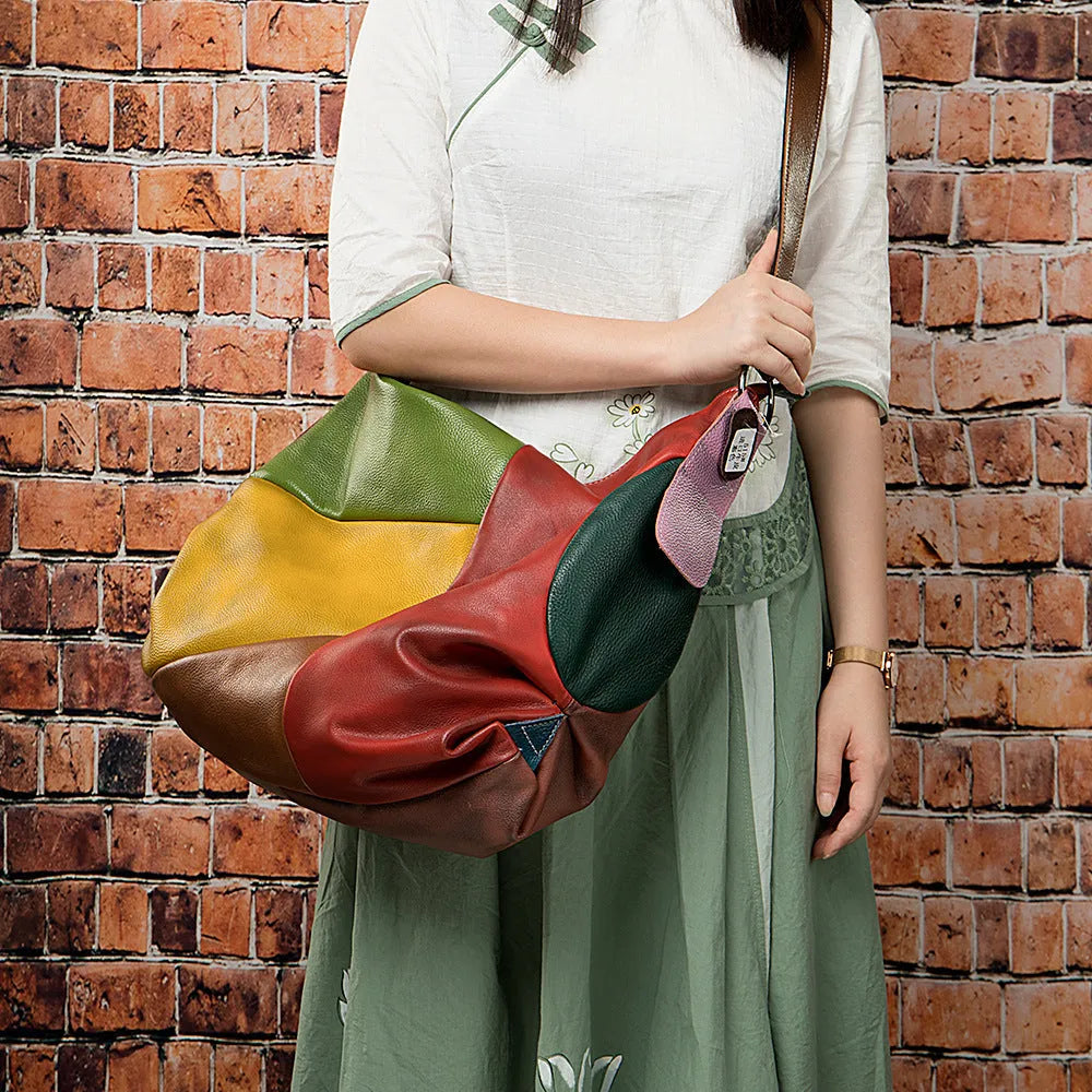 Brown cowhide leather travel bag with a long strap, shown next to a laptop and an A4 magazine for scale.