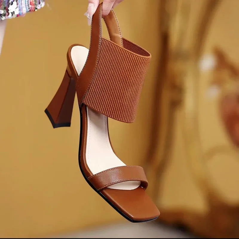 Women's black high heel sandals with a crossing elastic strap and a rubber sole.