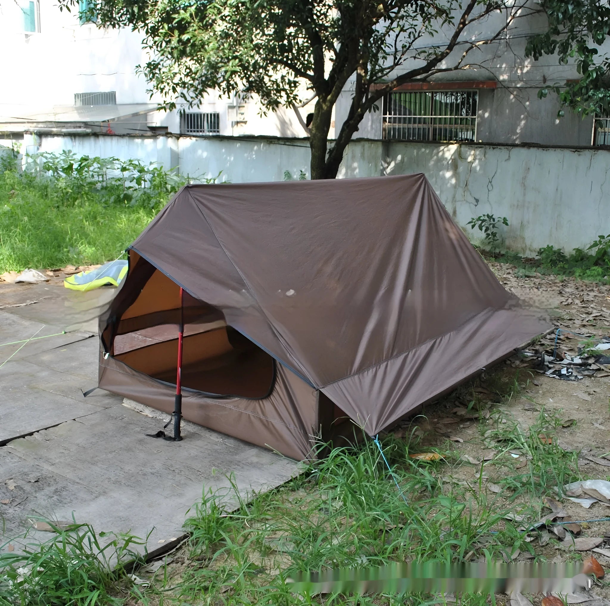 Brown ultralight A-frame hiking tent pitched with hiking poles in an outdoor setting