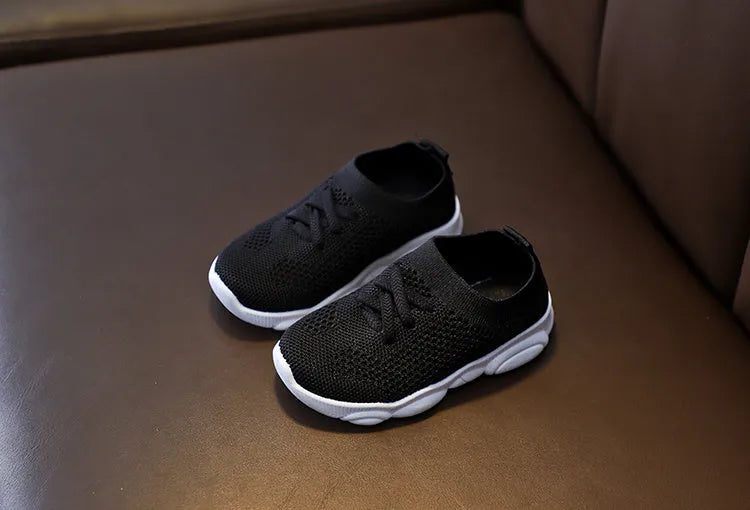 Children's white fabric lazy slip-on shoe with a non-slip rubber sole on a wooden floor.