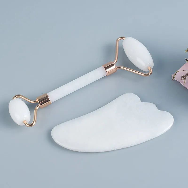 White jade facial roller with double heads and a matching gua sha scraping board on a plain surface.