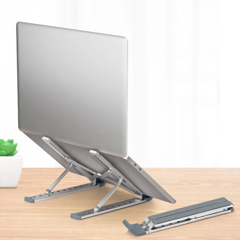 Silver adjustable folding laptop stand with hollow bottom and non-slip pads on a desk