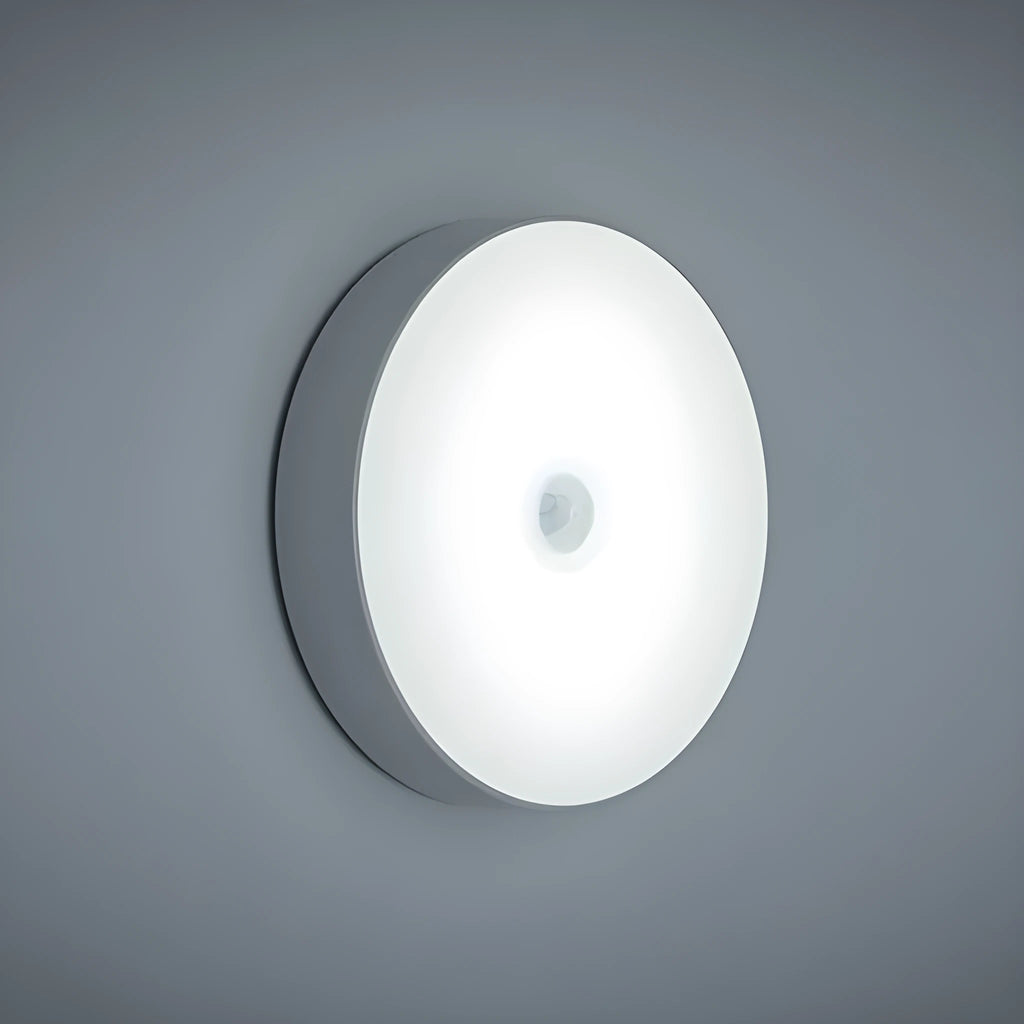 Compact white LED motion sensor night light with USB charging cable on a dark surface.