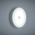 Compact white LED motion sensor night light with USB charging cable on a dark surface.