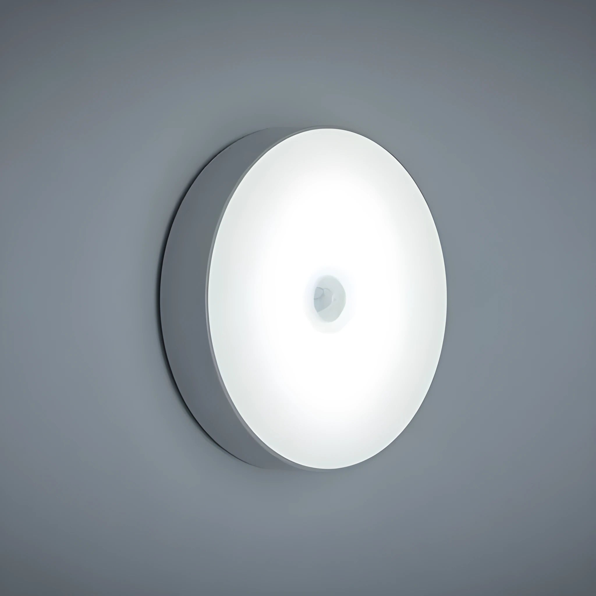 Compact white LED motion sensor night light with USB charging cable on a dark surface.