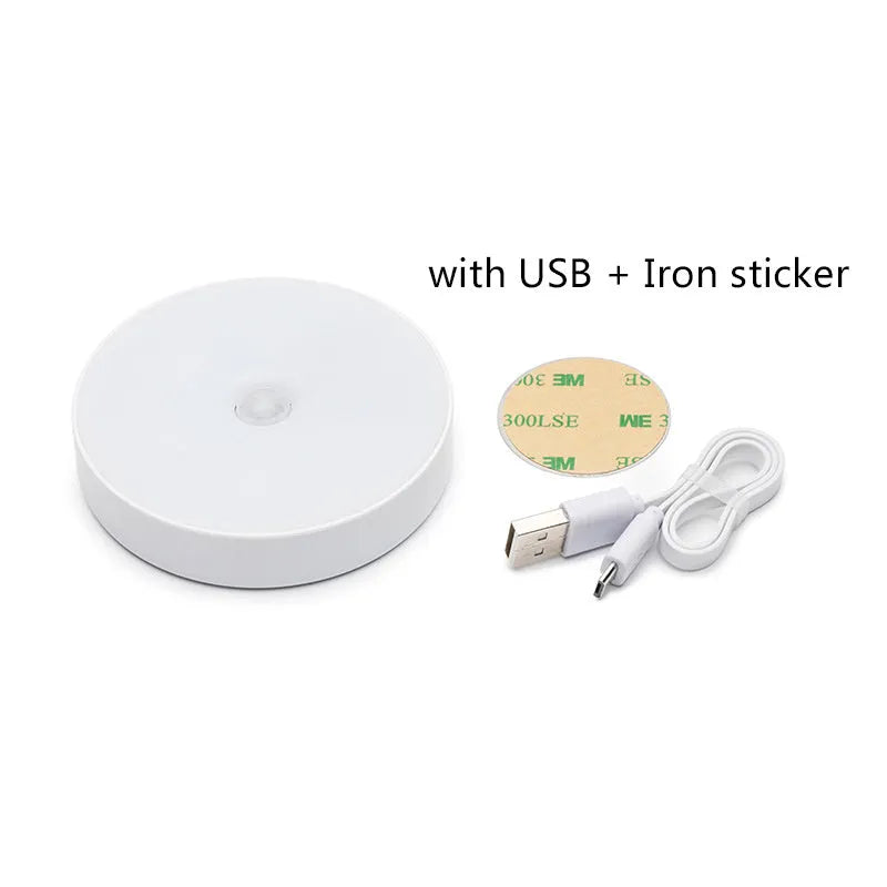 Compact white LED motion sensor night light with USB charging cable on a dark surface.