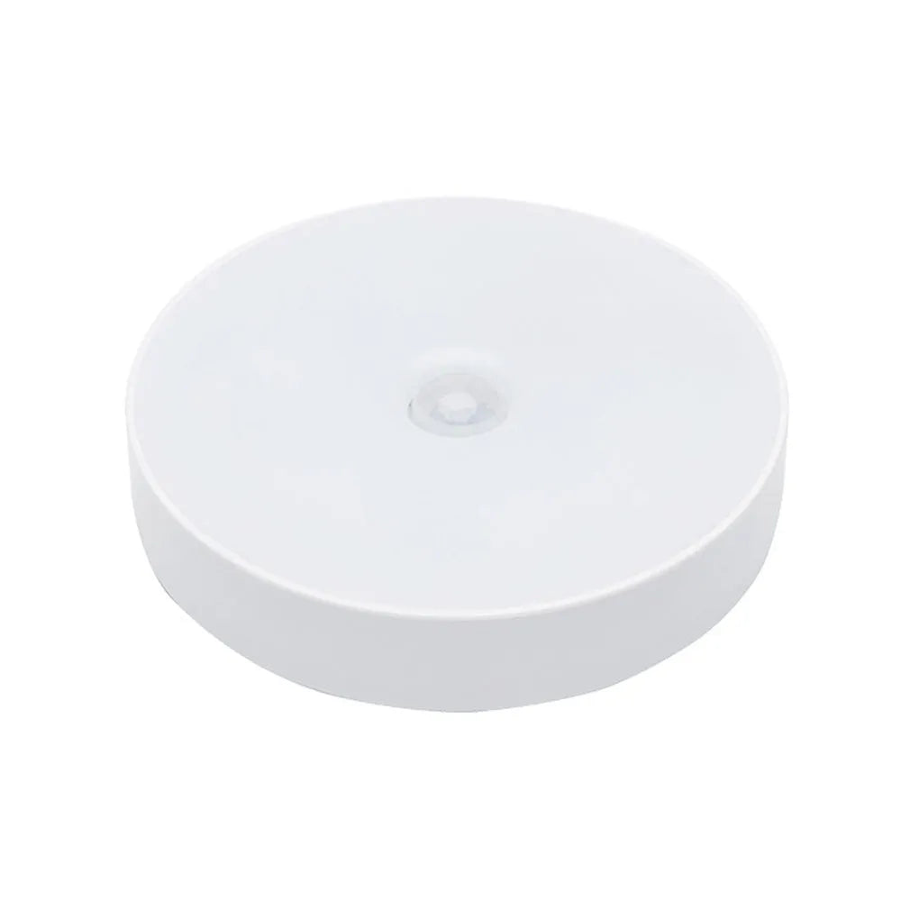 Compact white LED motion sensor night light with USB charging cable on a dark surface.