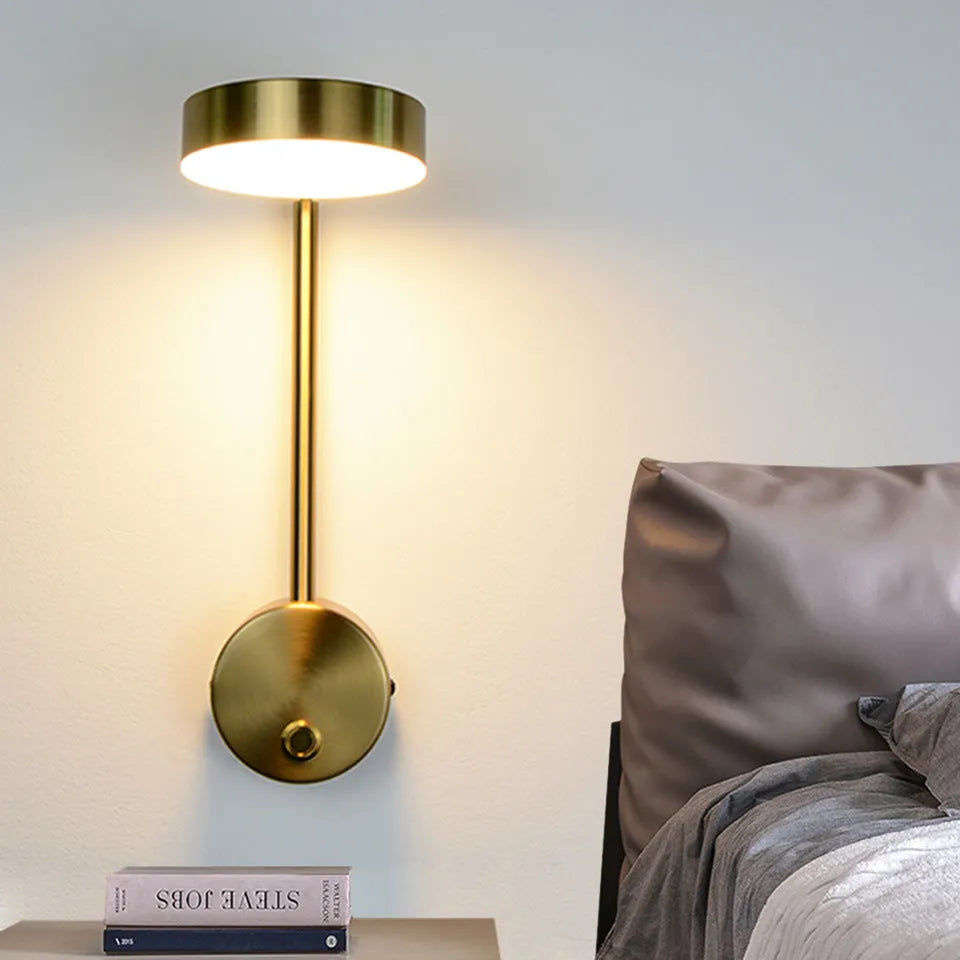 Gold LED wall lamp with rotary switch and acrylic shade on a wall