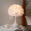 White feather table lamp with fabric shade on a wooden bedside table.
