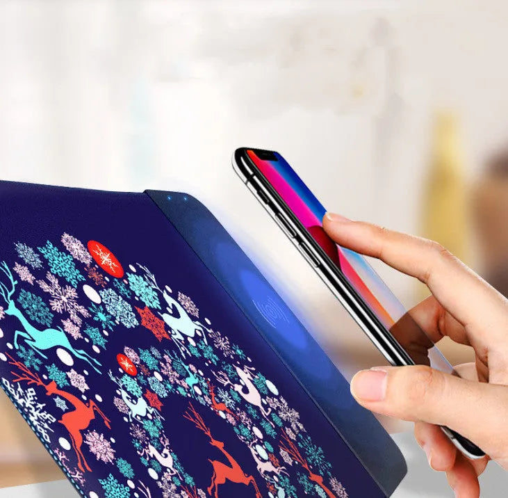 Black wireless charging mouse pad with RGB lighting edge and a cartoon design, shown on a desk.