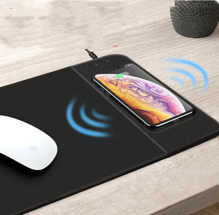 Black wireless charging mouse pad with RGB lighting edge and a cartoon design, shown on a desk.