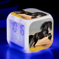 Small square cartoon-style LED alarm clock with colour-changing light feature on a table.