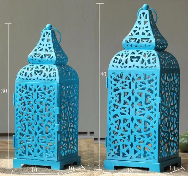 A blue iron Moroccan lantern candlestick with a hollow geometric design, shown next to a white and yellow pair.