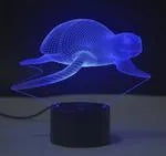 Small 3D acrylic LED table lamp on black base displaying multi-coloured gradient light, with remote control.