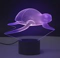Small 3D acrylic LED table lamp on black base displaying multi-coloured gradient light, with remote control.