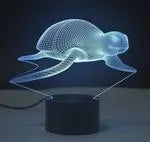 Small 3D acrylic LED table lamp on black base displaying multi-coloured gradient light, with remote control.