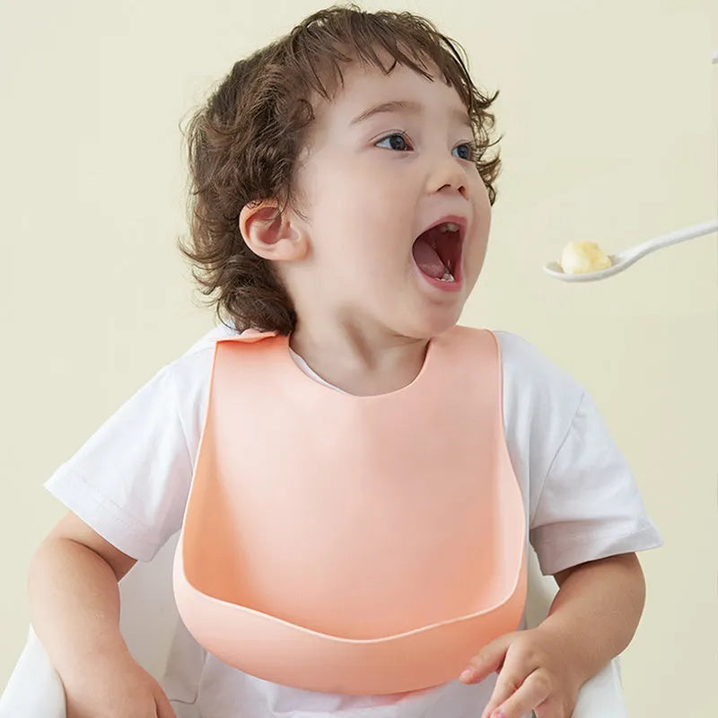 Soft waterproof silicone baby bib with food catcher in pink, with adjustable neck closure