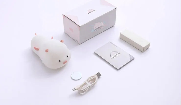 Blue silicone pig-shaped rechargeable LED night light with touch control on a wooden surface.