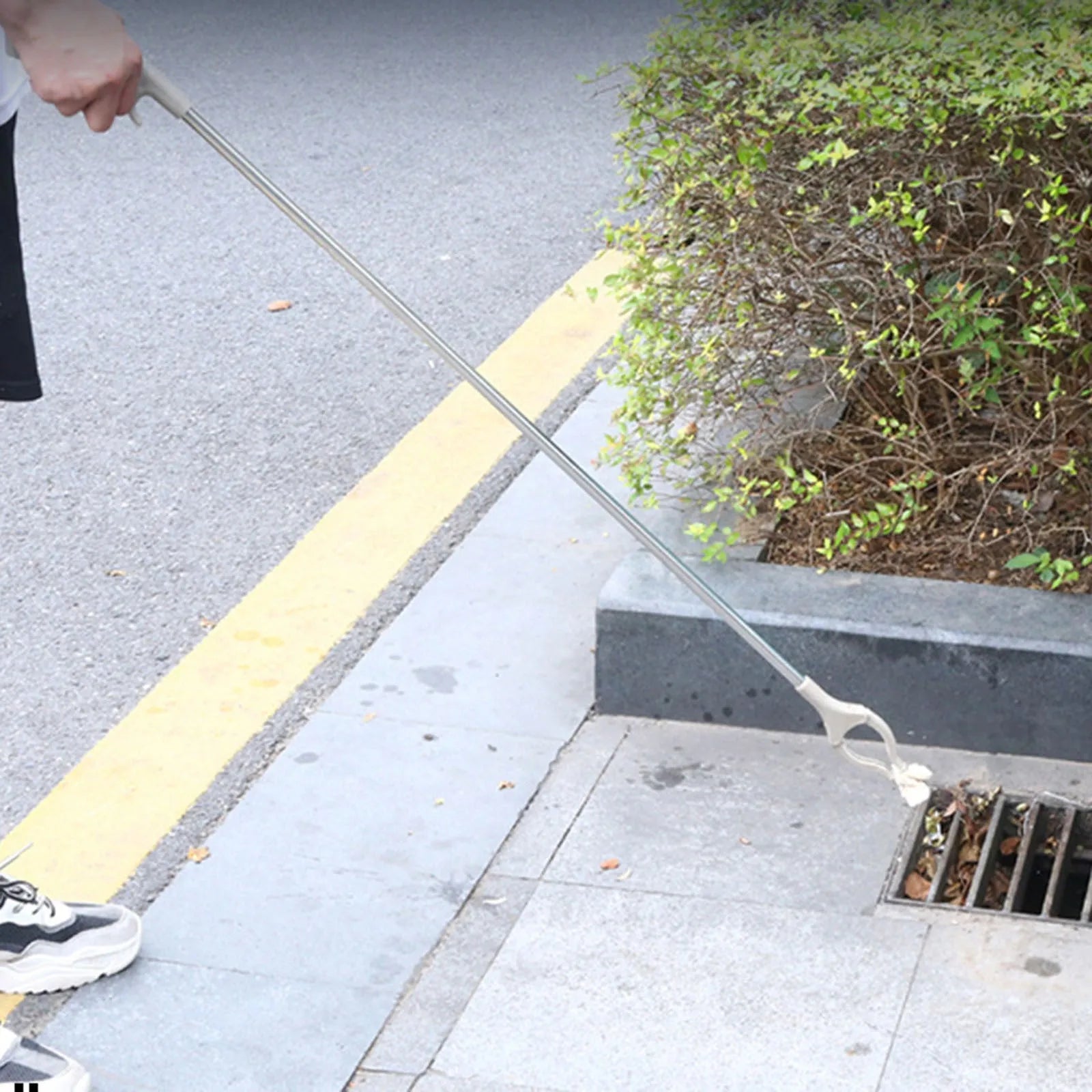 Stainless steel and plastic extended garbage picker tool with push handle and gripper jaws.