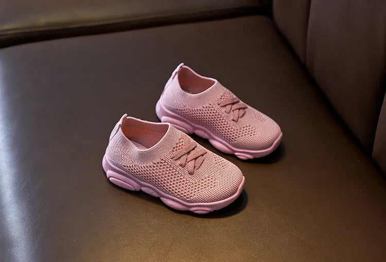Children's white fabric lazy slip-on shoe with a non-slip rubber sole on a wooden floor.