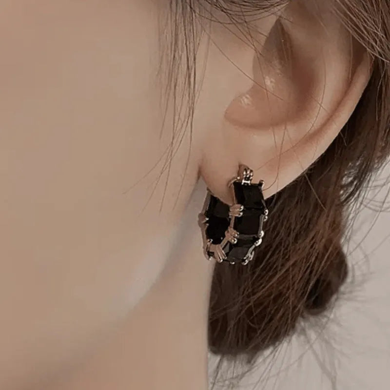 Women's geometric U-shaped gold earrings with round black zircon crystals on white background