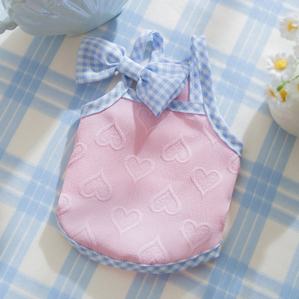 Small dog wearing a blue vest with a heart relief texture and white bow suspenders.