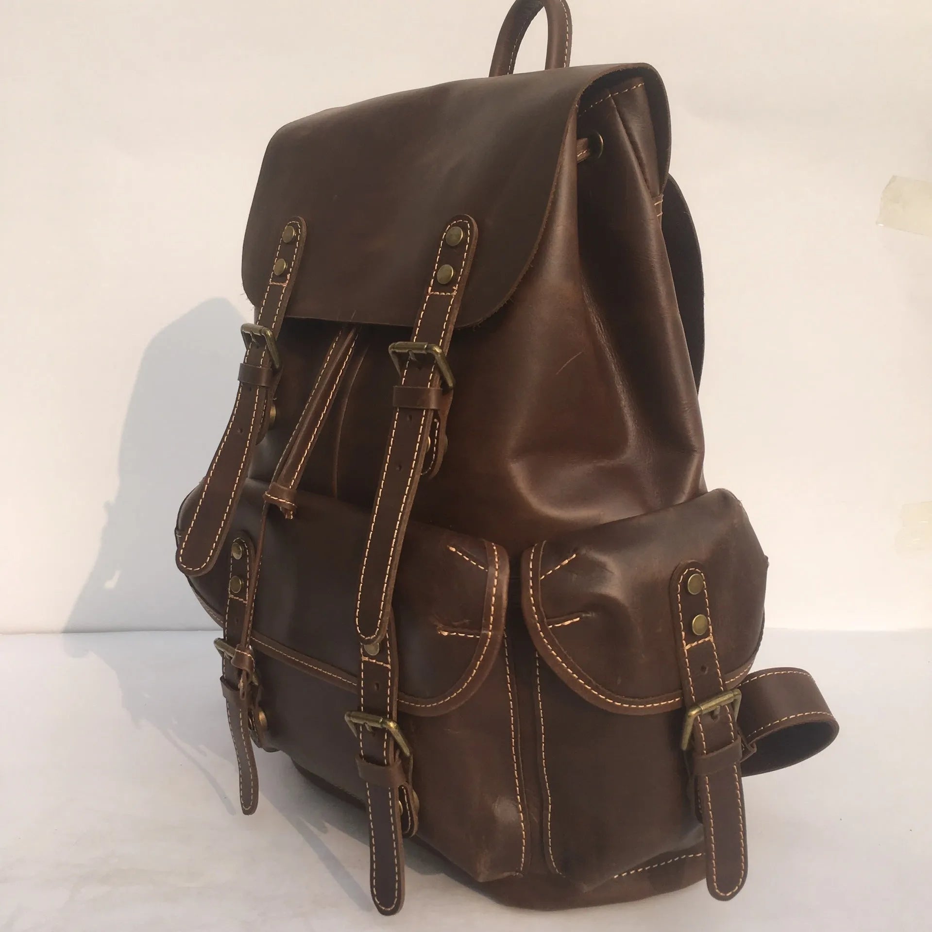 Brown men's leather backpack showing genuine cowhide material and integrated air pillow shoulder straps.