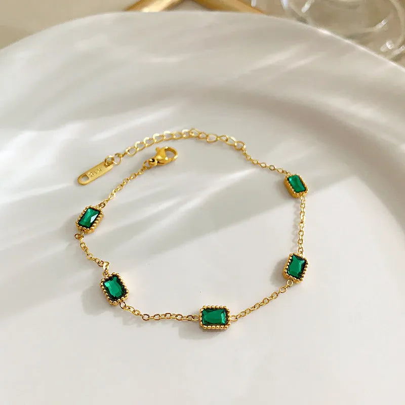 Titanium steel emerald zircon necklace and bracelet set with gold hardware and O-ring chain on a white background