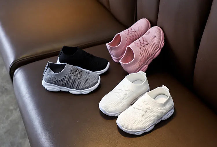 Children's white fabric lazy slip-on shoe with a non-slip rubber sole on a wooden floor.