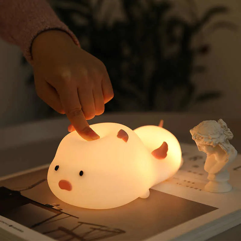 Blue silicone pig-shaped rechargeable LED night light with touch control on a wooden surface.